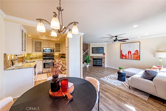 dining space with recessed lighting, light wood-style floors, ceiling fan with notable chandelier, a fireplace, and crown molding