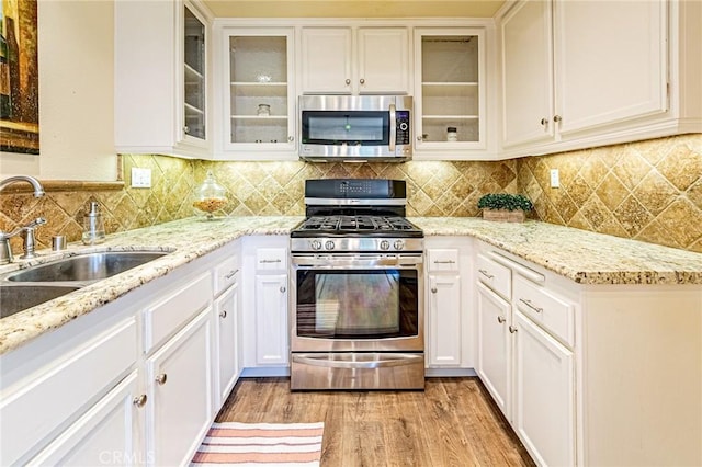 kitchen featuring white cabinets, appliances with stainless steel finishes, light wood-style flooring, and a sink