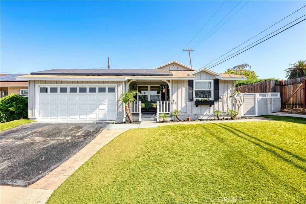 single story home with a front lawn, board and batten siding, roof mounted solar panels, fence, and a garage