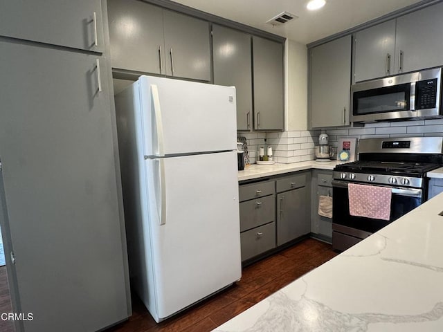 kitchen with decorative backsplash, stainless steel appliances, gray cabinetry, dark wood-type flooring, and visible vents