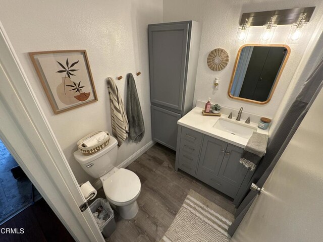 bathroom featuring toilet, vanity, wood finished floors, and baseboards