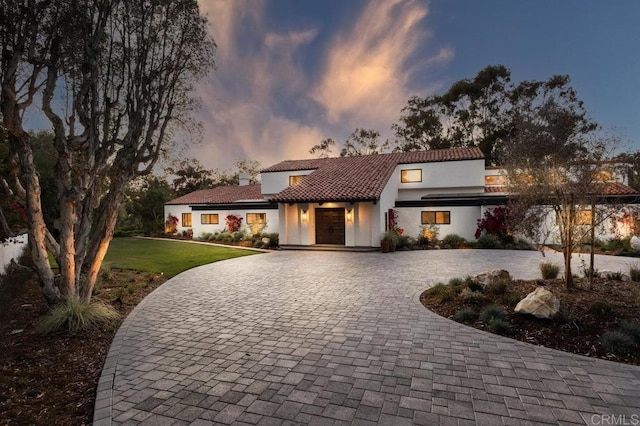 view of front of property featuring a tile roof, a front yard, curved driveway, and stucco siding