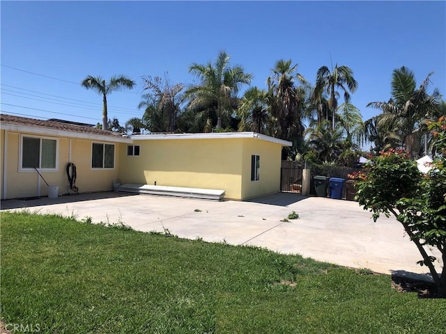 back of house with fence, stucco siding, a yard, and a patio area