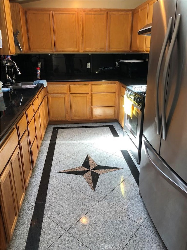 kitchen with dark countertops, a sink, granite finish floor, stainless steel appliances, and under cabinet range hood