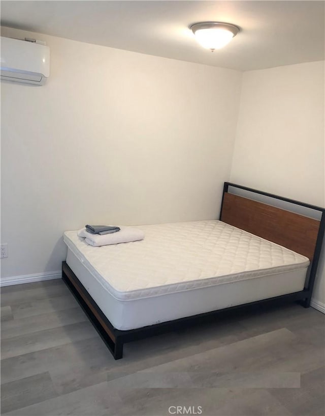 bedroom with baseboards, a wall unit AC, and wood finished floors