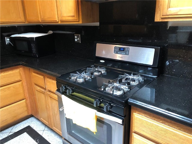 kitchen with black microwave, dark stone counters, brown cabinetry, and stainless steel gas range oven