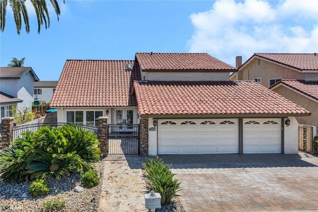 view of front of home featuring an attached garage, a tiled roof, stucco siding, decorative driveway, and a gate