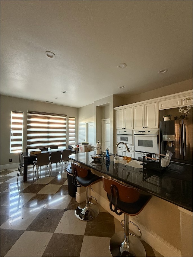 kitchen with fridge with ice dispenser, baseboards, dark countertops, and a breakfast bar