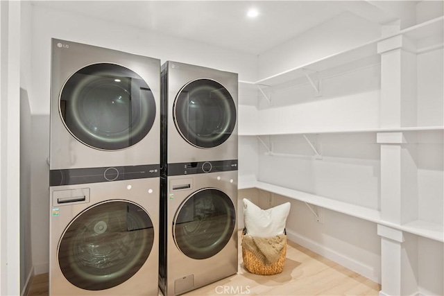 washroom featuring stacked washer / drying machine, wood finished floors, baseboards, and laundry area