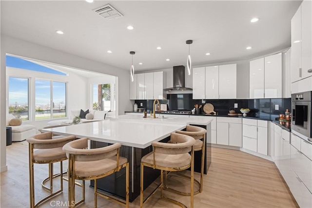 kitchen with wall chimney exhaust hood, white cabinets, stainless steel appliances, visible vents, and modern cabinets