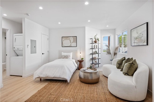 bedroom featuring recessed lighting, light wood-style floors, stacked washer and dryer, and electric panel