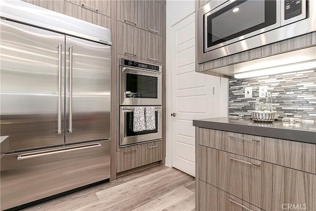 20512 W Esmeralda Ln, Porter Ranch, CA 91311 - kitchen with built in appliances, dark countertops, backsplash, light wood-type flooring, and modern cabinets