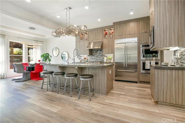 20512 W Esmeralda Ln, Porter Ranch, CA 91311 - kitchen with appliances with stainless steel finishes, exhaust hood, backsplash, a breakfast bar area, and a chandelier