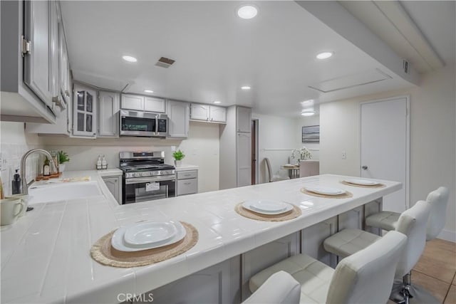 kitchen featuring stainless steel appliances, a peninsula, a sink, visible vents, and tile counters