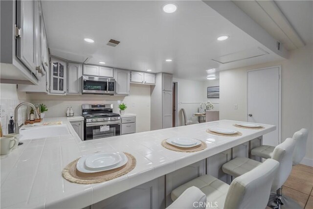 11249 Ferina St, Norwalk, CA 90650 - kitchen featuring stainless steel appliances, tile counters, a sink, a peninsula, and recessed lighting