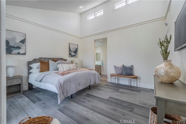 bedroom featuring baseboards, ensuite bath, wood finished floors, and a high ceiling