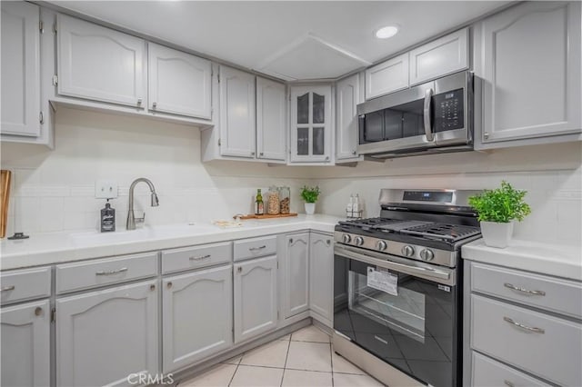 kitchen featuring a sink, light tile patterned flooring, glass insert cabinets, light countertops, and appliances with stainless steel finishes