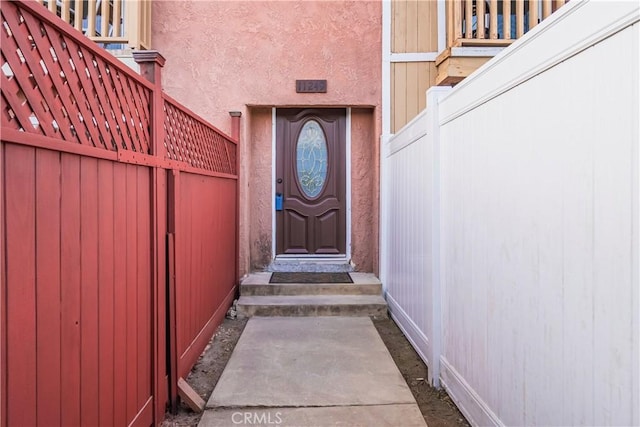view of exterior entry featuring fence and stucco siding