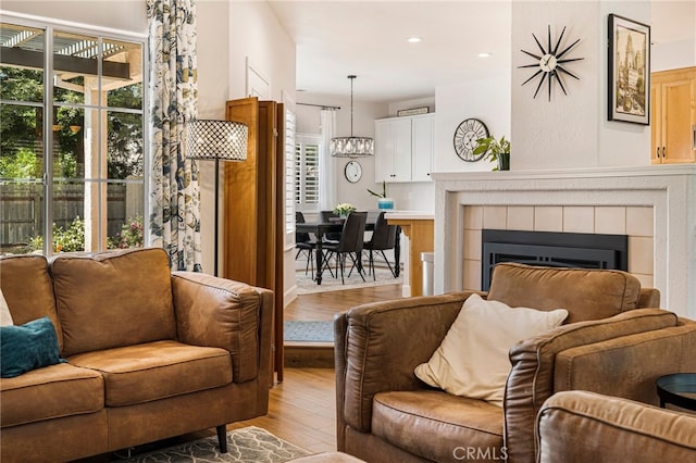 living room featuring recessed lighting, light wood-style flooring, a tile fireplace, and an inviting chandelier