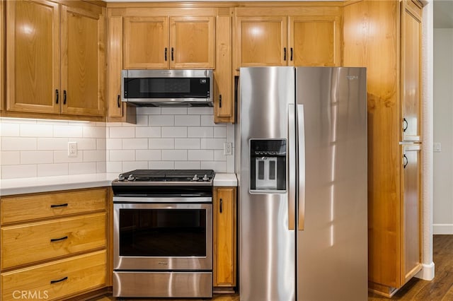 kitchen with stainless steel appliances, light countertops, brown cabinetry, tasteful backsplash, and dark wood-style flooring