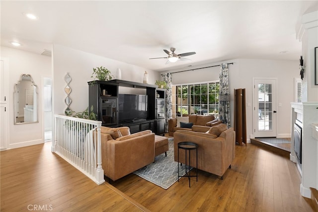 living area featuring ceiling fan, a glass covered fireplace, wood-type flooring, and visible vents