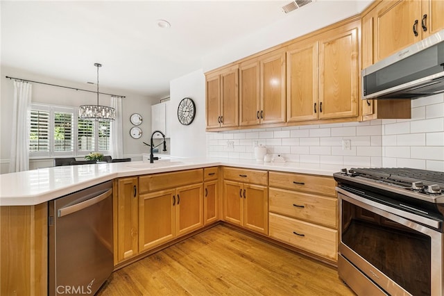 kitchen with a sink, light wood-style floors, a peninsula, appliances with stainless steel finishes, and visible vents