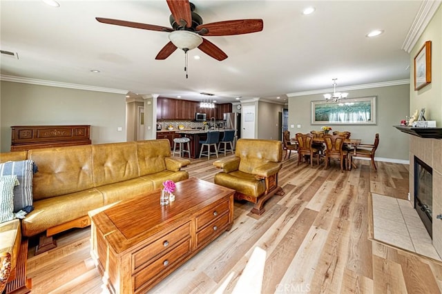 living area with recessed lighting, light wood finished floors, a tiled fireplace, ornamental molding, and ceiling fan with notable chandelier