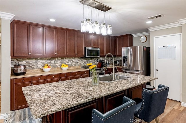 kitchen featuring a sink, stainless steel appliances, crown molding, a breakfast bar area, and visible vents
