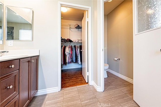 full bathroom with toilet, a walk in closet, vanity, and baseboards