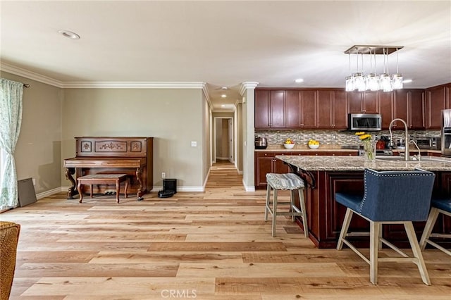 kitchen with light stone countertops, stainless steel microwave, light wood finished floors, a kitchen breakfast bar, and crown molding
