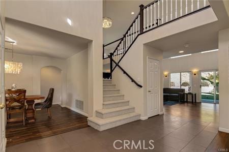 stairs with arched walkways, a high ceiling, tile patterned floors, and a notable chandelier
