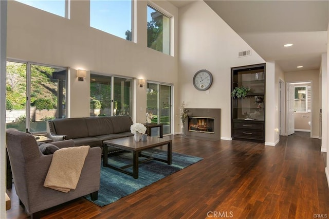 living area with a towering ceiling, wood finished floors, visible vents, and plenty of natural light