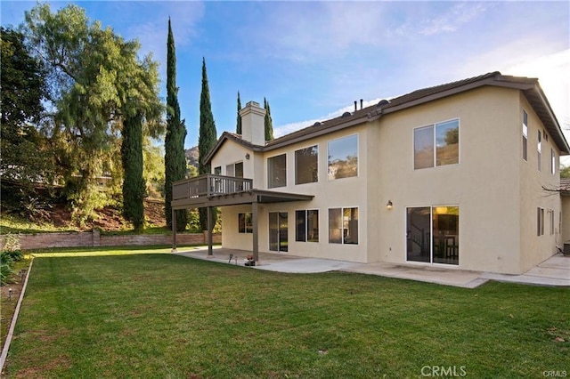 back of property featuring a lawn, a chimney, a patio, and stucco siding