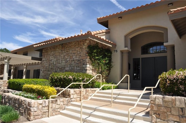 view of exterior entry with a pergola, stone siding, a tiled roof, and stucco siding