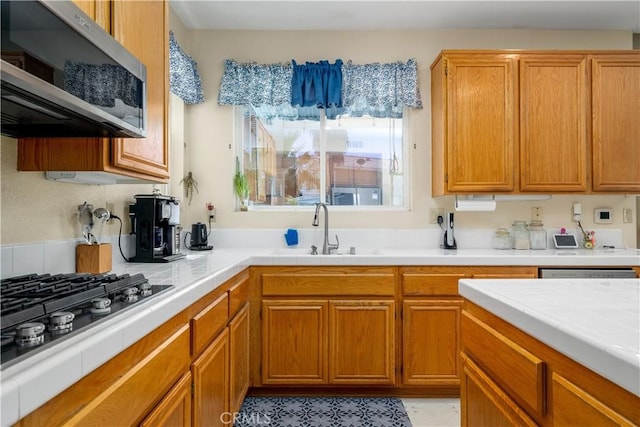 kitchen featuring gas cooktop, a sink, stainless steel microwave, brown cabinetry, and tile counters
