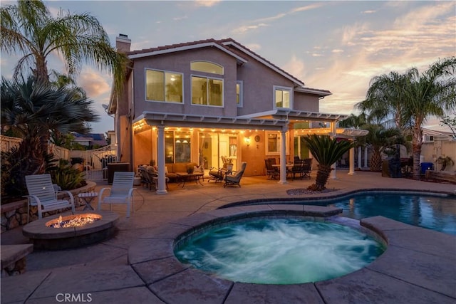 back of property with a chimney, stucco siding, a patio area, an outdoor living space with a fire pit, and a pool with connected hot tub