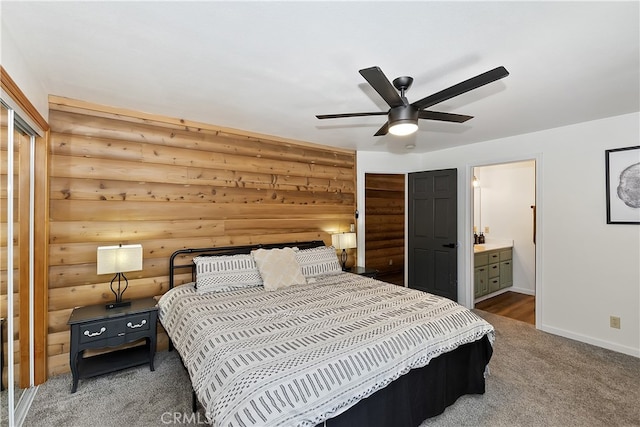 carpeted bedroom with ensuite bathroom, baseboards, rustic walls, and ceiling fan
