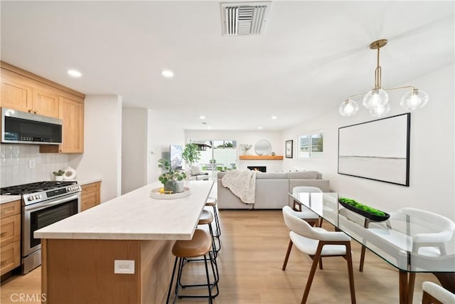 kitchen featuring appliances with stainless steel finishes, light brown cabinets, backsplash, a kitchen island, and visible vents