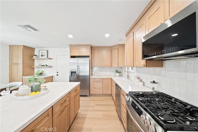 kitchen featuring appliances with stainless steel finishes, light brown cabinets, light wood-style flooring, backsplash, and visible vents