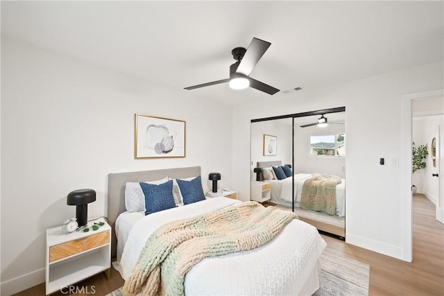 bedroom with a ceiling fan, baseboards, wood finished floors, visible vents, and a closet