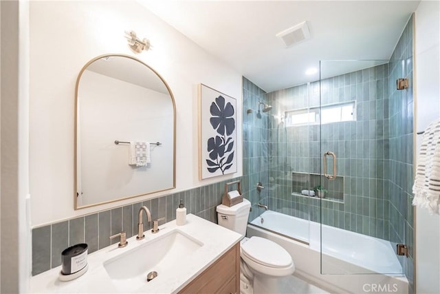 full bathroom featuring vanity, toilet, enclosed tub / shower combo, tile walls, and visible vents