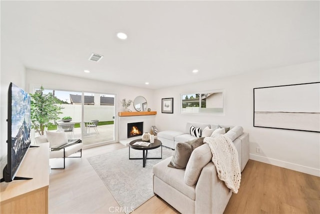 living room featuring visible vents, light wood-style floors, recessed lighting, baseboards, and a lit fireplace
