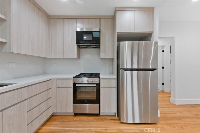 kitchen with light brown cabinets, modern cabinets, light wood finished floors, light countertops, and appliances with stainless steel finishes