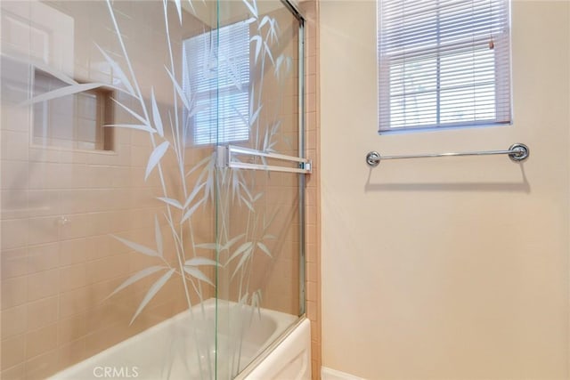 bathroom featuring baseboards and bath / shower combo with glass door