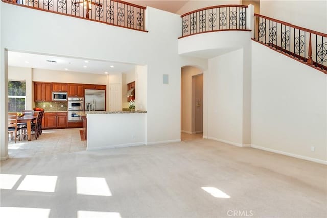 unfurnished living room featuring arched walkways, baseboards, light colored carpet, and a towering ceiling