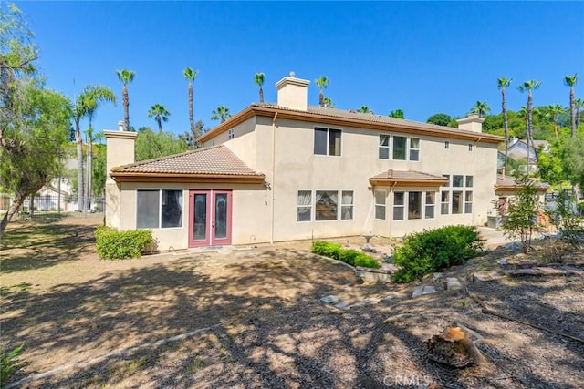 rear view of property with a tiled roof, a chimney, stucco siding, and french doors