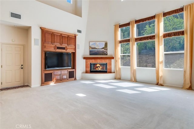 unfurnished living room featuring visible vents, a glass covered fireplace, light carpet, baseboards, and a high ceiling