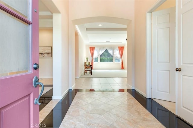 interior space with arched walkways, tile patterned floors, baseboards, and a raised ceiling