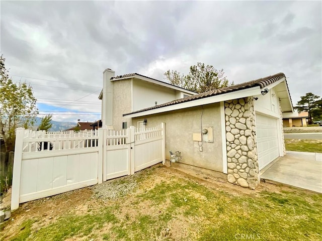 1078 W King St, Banning, CA 92220 - view of side of home with a garage, a tiled roof, concrete driveway, stucco siding, and fence