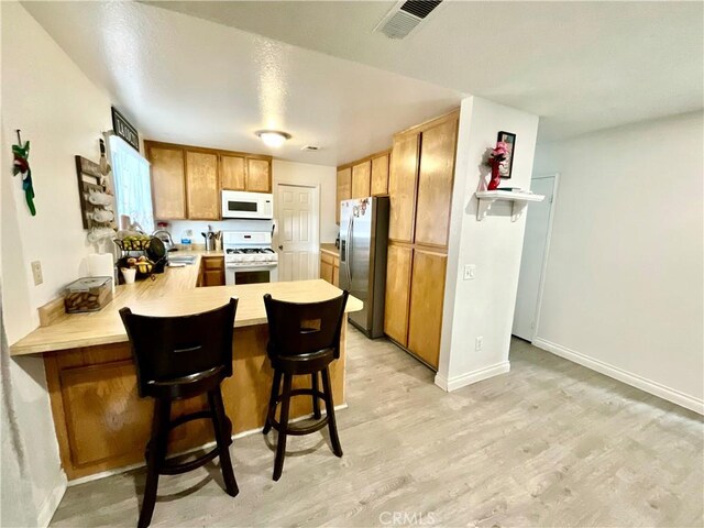 1078 W King St, Banning, CA 92220 - kitchen featuring visible vents, light countertops, light wood finished floors, white appliances, and a peninsula